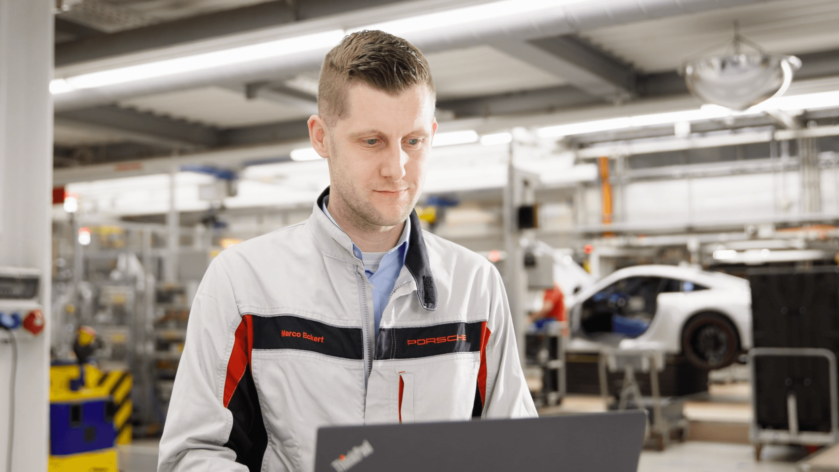 Porsche-Mitarbeiter konfiguriert auf dem Shopfloor einen digitalen Workflow am Laptop vor einem Auto auf der Montagelinie