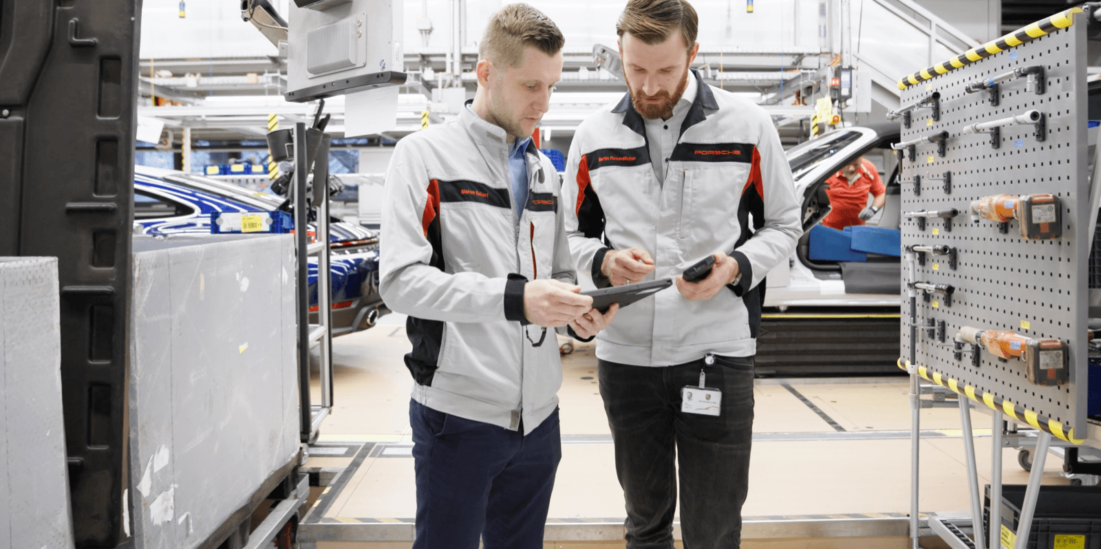 Zwei Porsche-Mitarbeiter prüfen digitale Arbeitsanweisungen auf einem Tablet an einer Montagestation