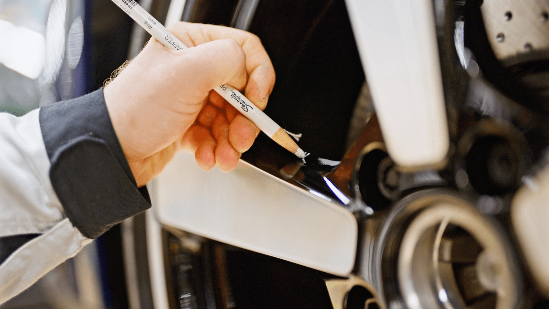 Close-up of an inspector marking a surface finding beside a vehicle wheel during in-process inspection