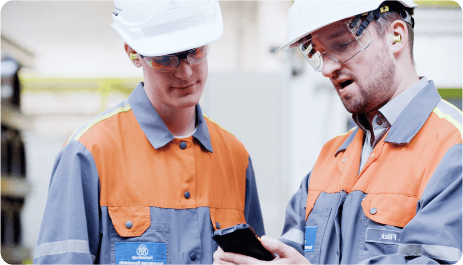 Two operators on a shop floor reviewing tasks on a mobile device.